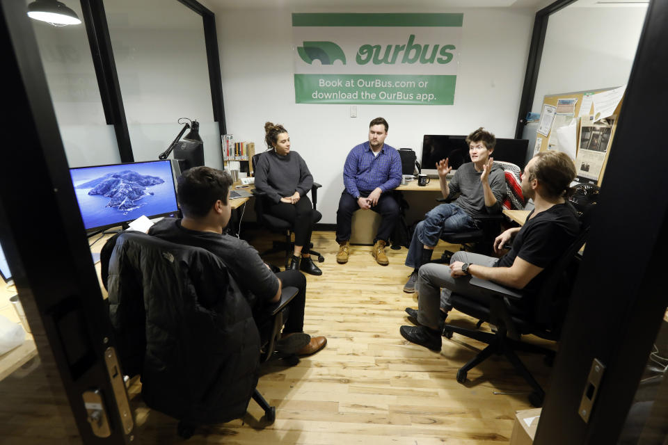 In this Monday, Nov. 4, 2019 photo, from left to right, Steve Motino, Lea Knio, Samuel Brownsword, Axel Hellman and Anthony Giordano, of OurBus, meet in their WeWork office space, in New York. WeWork is slashing the lavish spending that fueled the office-sharing company’s breakneck growth while racking up unsustainable losses that ultimately turned off Wall Street investors, forcing it to shelve its initial public offering. For now, many of its members are rooting for the company, including Hellman. “It’s easy to poke fun at the motivational signage and fruit water,” Hellman said. “But in reality, it’s the network available to us through WeWork and the flexibility they offer that makes the company valuable to us.” (AP Photo/Richard Drew)