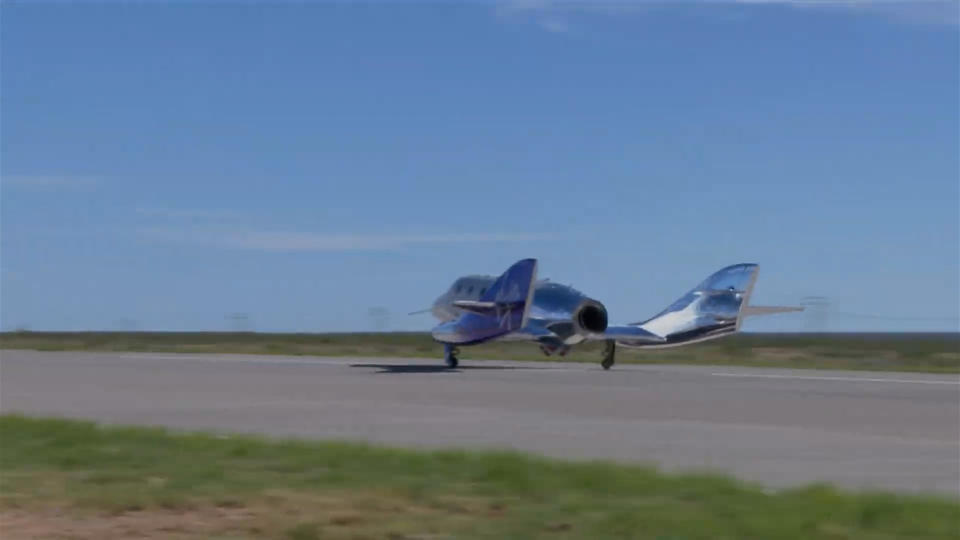 a silvery space plane on a runway beneath a blue sky.