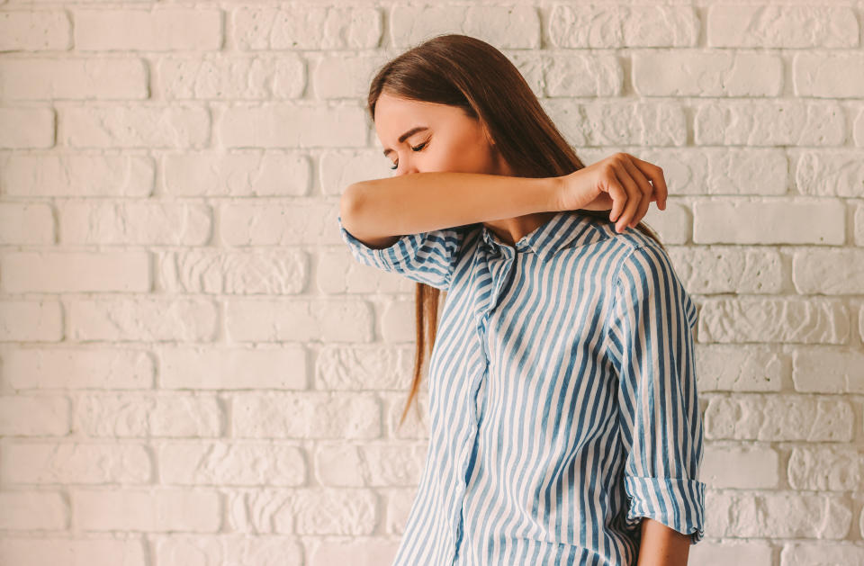 Young ill woman covering her nose and mouth with arm while sneezing at home. Sick infected girl patient coughing in her elbow. Coronavirus COVID-19 symptoms. Virus protection. Correct cough in hand