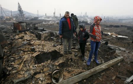 Local residents stand amidst the debris of a burnt building in the settlement of Shyra, damaged by recent wildfires, in Khakassia region, April 13, 2015. REUTERS/Ilya Naymushin