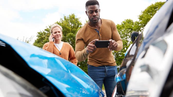 Male Motorist Involved In Car Accident Taking Picture Of Damage For Insurance Claim.