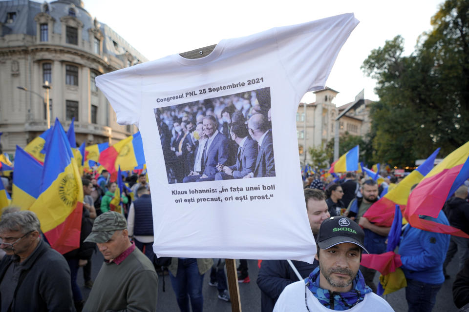 A man holds a t-shirt with a picture showing Romania's president Klaus iohannis at the ruling Liberal Party congress that reads : "Klaus Iohannis - In front of a disease you are either careful or stupid" during an anti-government protest organised by the far-right Alliance for the Unity of Romanians or AUR, in Bucharest, Romania, Saturday, Oct. 2, 2021. Thousands took to the streets calling for the governments resignation, as Romania reported 12.590 new COVID-19 infections in the past 24 hour interval, the highest ever daily number since the start of the pandemic. (AP Photo/Vadim Ghirda)