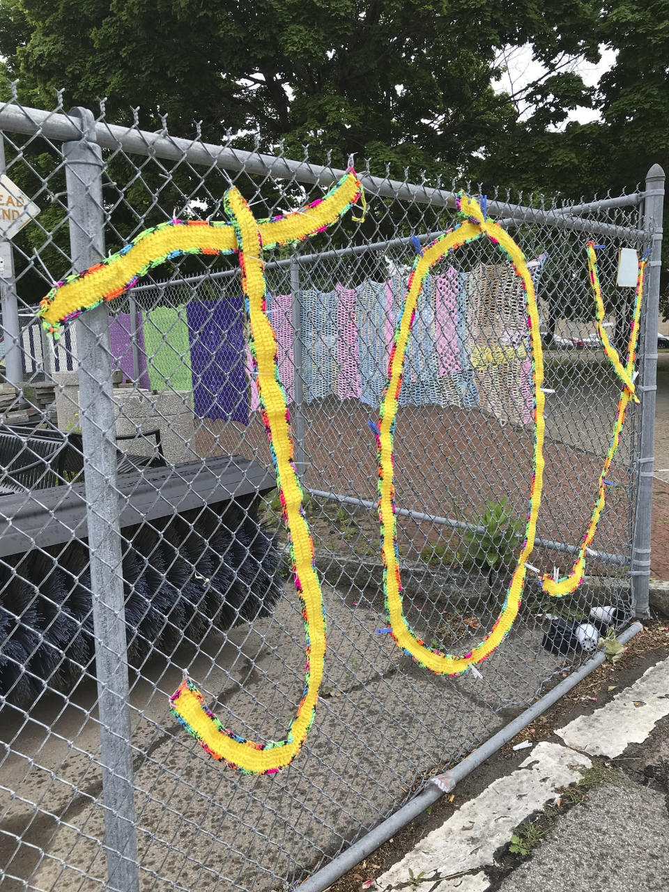 This June 2018 photo provided by Hinda Mandell shows a yarn installation at Schiller Park in Rochester, N.Y. More than 40 women from Rochester participated in "Yarn at Schiller Park," a community event organized by Mandell to spruce up Schiller Park. Dozens of knit and crocheted blankets decorated chain-link fencing to bring color to a neglected park that bordered an outdoor storage space for the city's construction equipment. Knitters and crocheters call it yarn bombing. They're using fiber arts to make political statements, or maybe just to lift people's spirits. Experts say yarn bombing is part of a long tradition in which women use textile arts to agitate, excite or inspire. (Hinda Mandell via AP)
