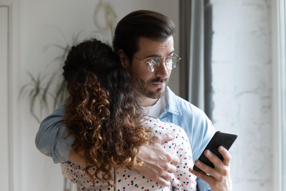 Man hugging female partner while checking his phone