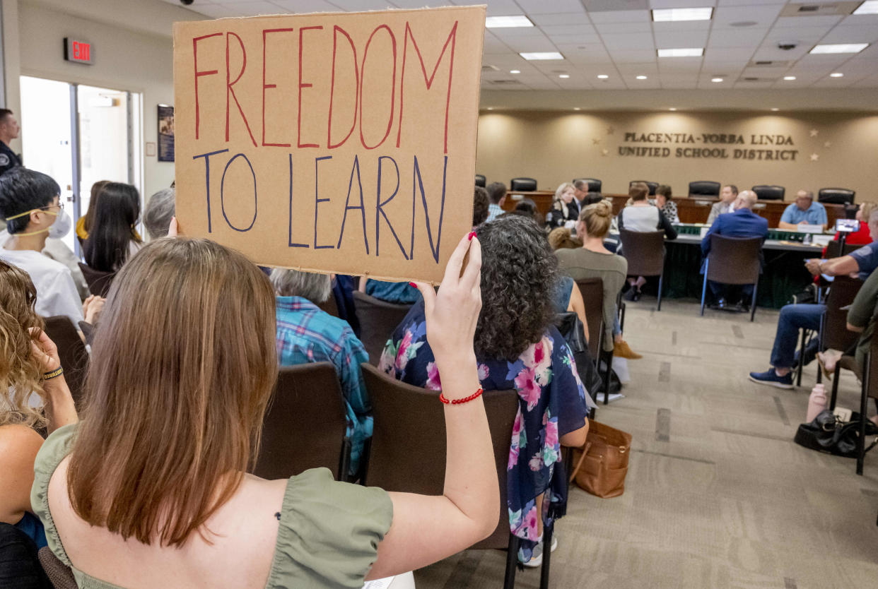 A woman at a school board meeting holds up a sign reading 