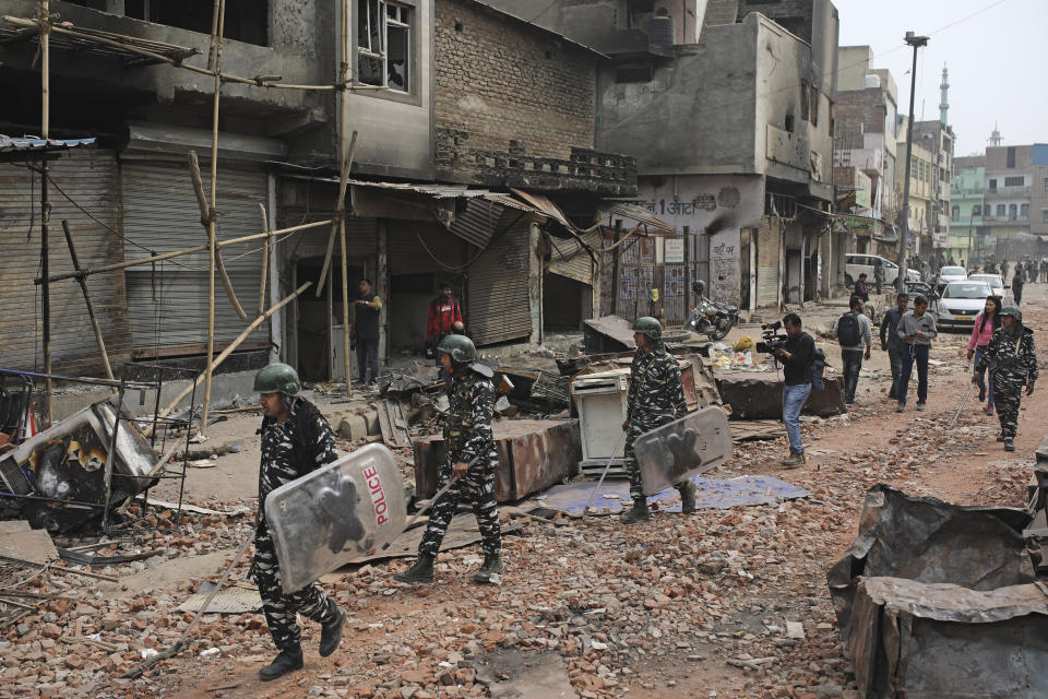 In this Thursday, Feb. 27, 2020, a video-journalist films as Indian paramilitary soldiers patrol a street vandalized in Tuesday's violence in New Delhi, India. Reporting in India has never been without its risks, but journalists say attacks on the press during last week's deadly communal riots between Hindus and Muslims in New Delhi show the situation is deteriorating. (AP Photo/Altaf Qadri)