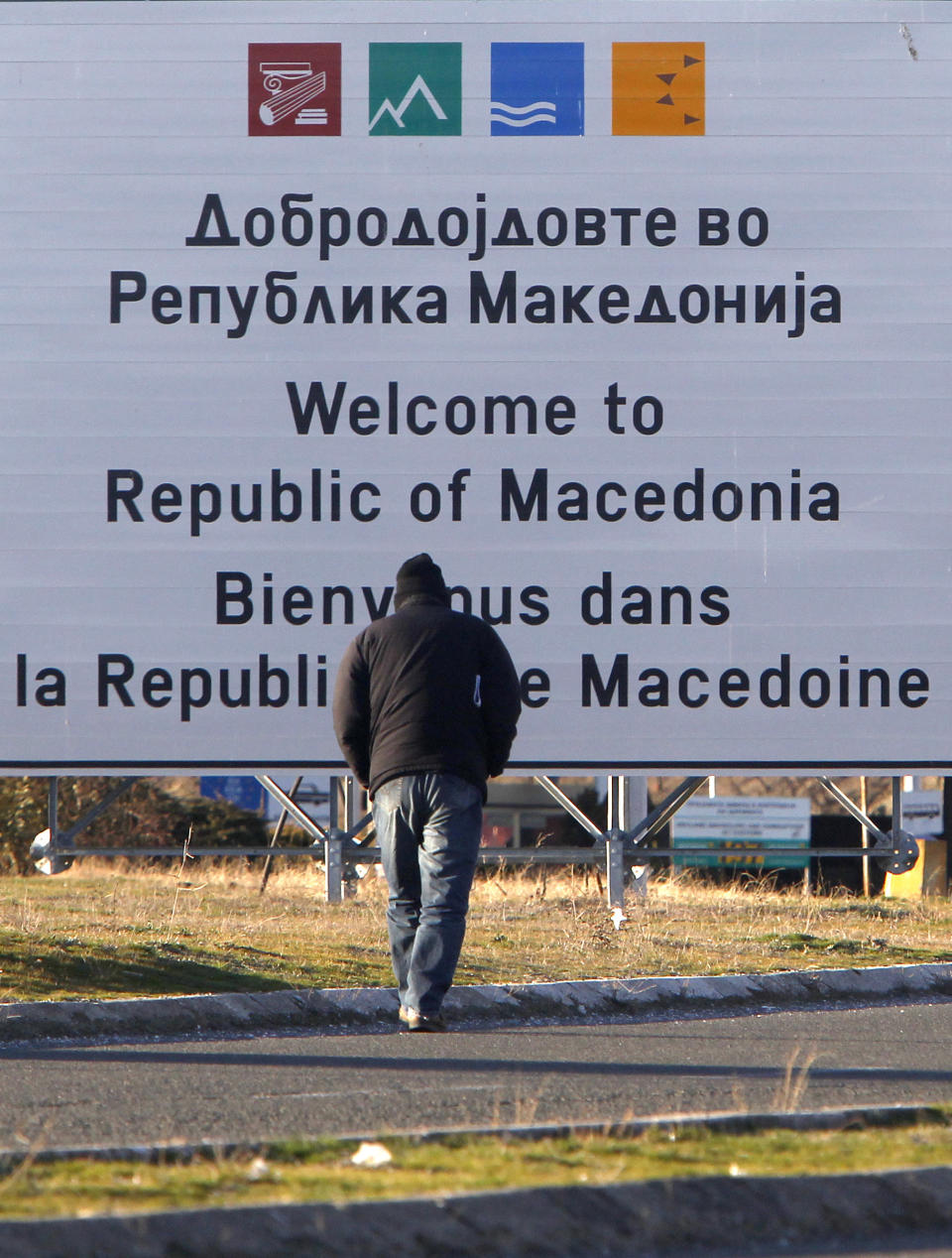 A man walks towards a welcome sign at Bogorodica border crossing, on Macedonia's southern border with Greece, Tuesday, Feb. 12, 2019. Macedonian authorities began Monday removing official signs from government buildings to prepare for the country's new name: North Macedonia. (AP Photo/Boris Grdanoski)