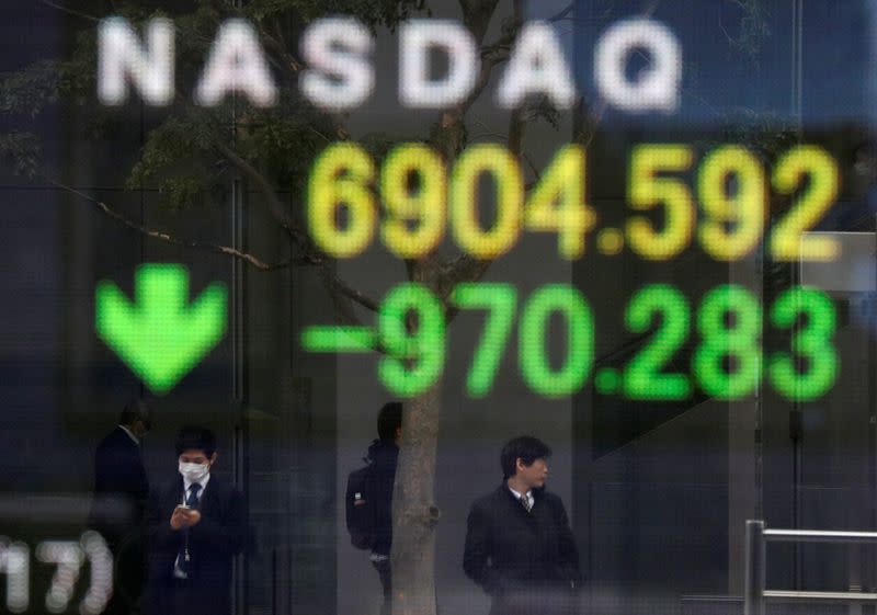 Passersby wearing protective face masks are reflected on a screen displaying NASDAQ movements outside a brokerage in Tokyo