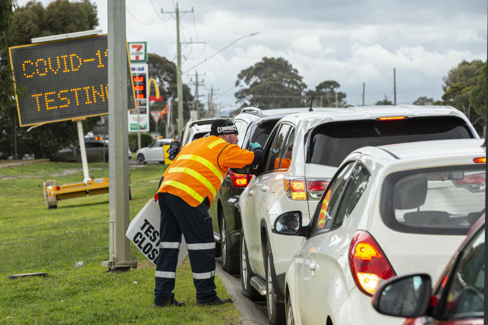 A man holding a sign saying ‘testing closed’ directs cars outside a COVID-19 testing site at Craigieburn Health in Melbourne, Tuesday, June 23, 2020.