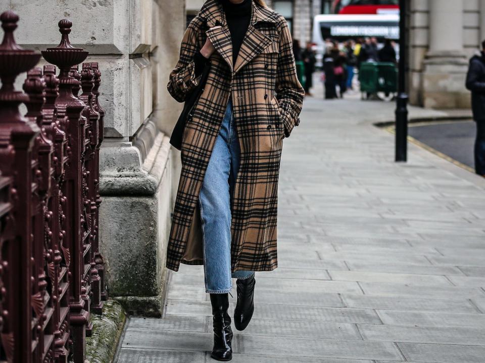 woman walking down a london street wearing a long plaid coat over jeans and a black shirt