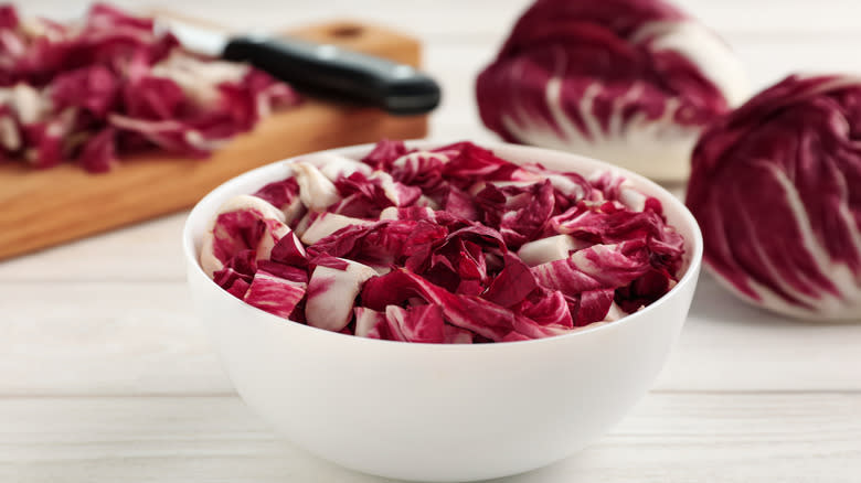 sliced radicchio in white bowl next to full heads of radicchio and cutting board