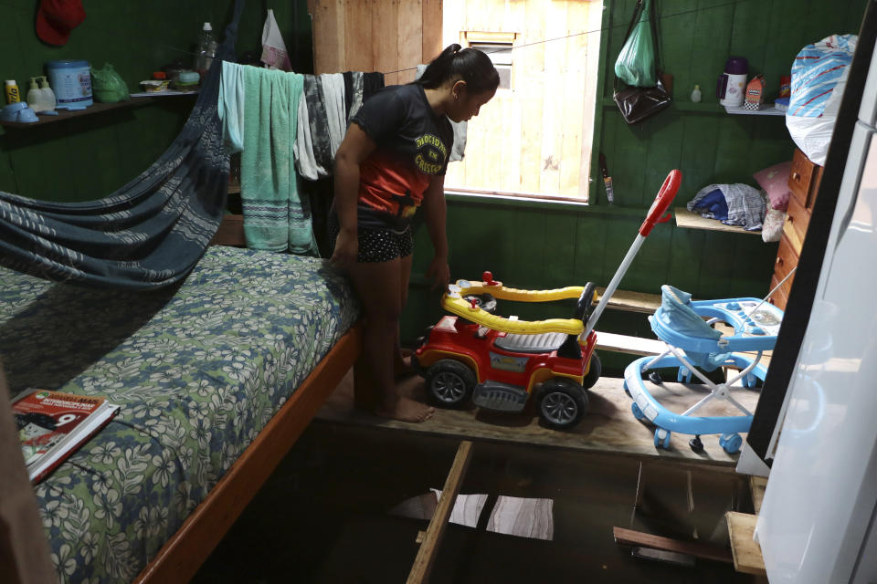 Valeria Ribeiro de Souza walks on a wooden plank that keeps furniture above floodwater inside her home in Anama, Amazonas state, Brazil, Thursday, May 13, 2021. (AP Photo/Edmar Barros)