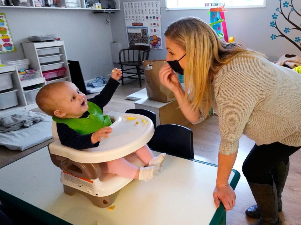 woman with a mask on signing about eating food to baby in a high chair