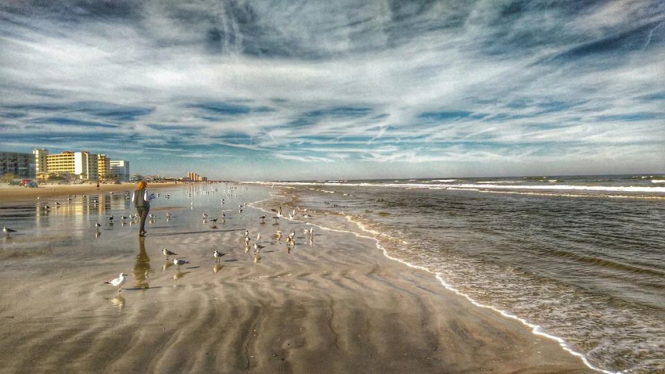 woman by seagulls on beach against cloudy sky