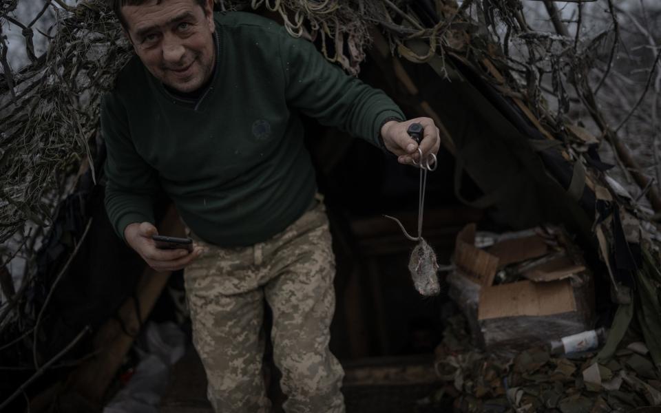A Ukrainian medic smiles as he carries a dead mouse out of a trench by the tail