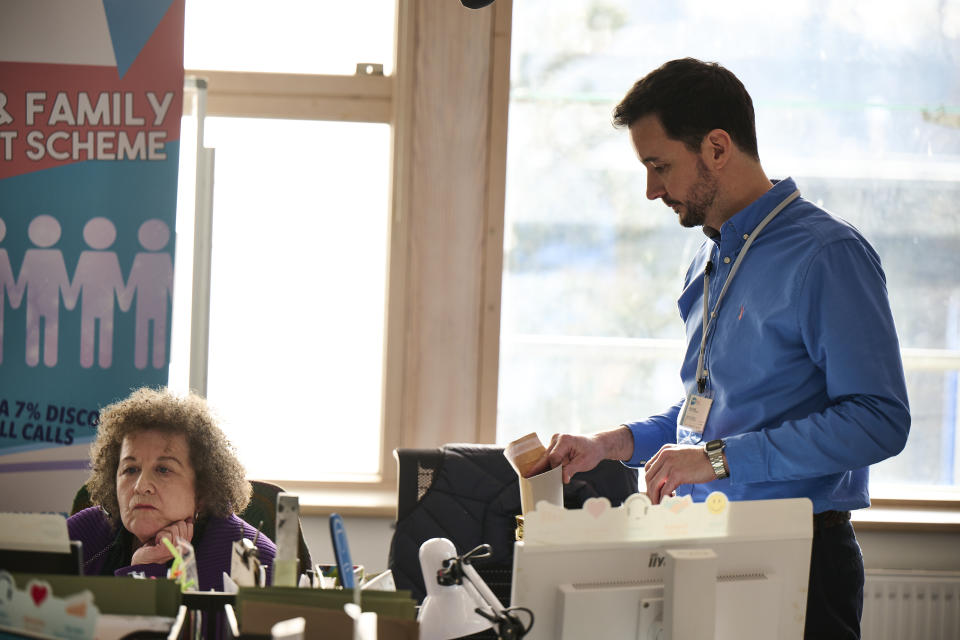 Mark (Sam Swainsbury) stands on the call centre floor holding an open A4 envelope, while Donna (Nicky Goldie) is on a call next to him