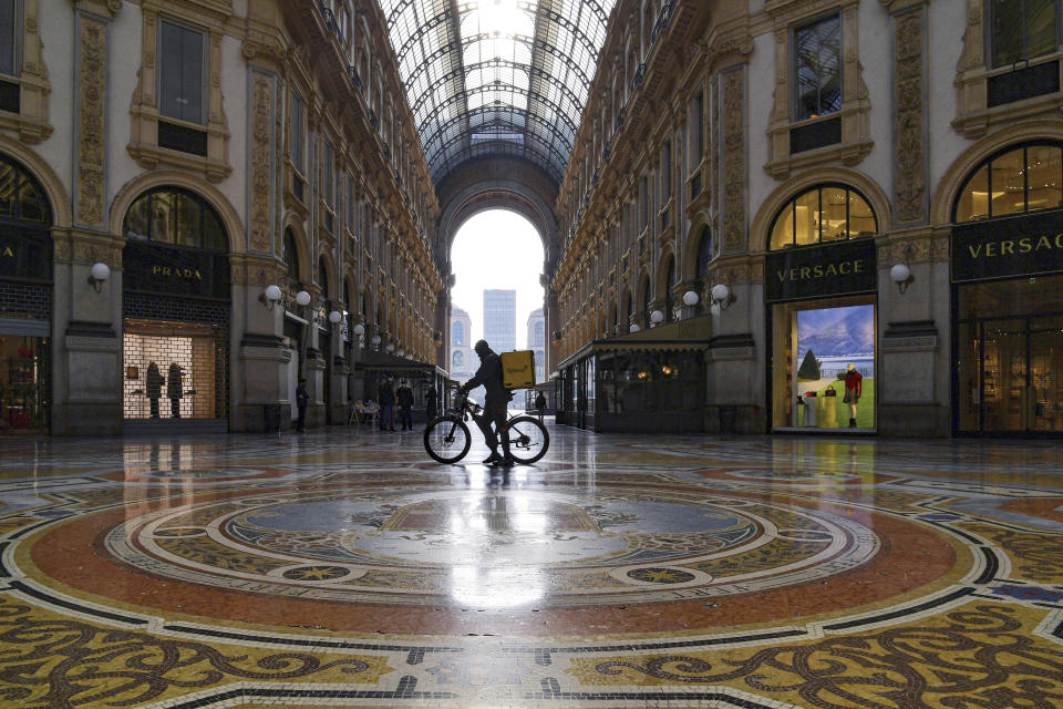 FILE - In this Nov. 6, 2020 file photo, a food delivery rider pushes his bicycle inside the Vittorio Emanuele shopping arcade in Milan, Italy. Italy is cracking down on bike delivery service companies, with one Milan prosecutor saying the riders, most of them immigrants, are practically treated like slaves. Milan prosecutors on Wednesday told a news conference that four delivery companies in Italy have been given 90 days to improve their treatment of riders. (Gian Mattia D'Alberto/LaPresse via AP)