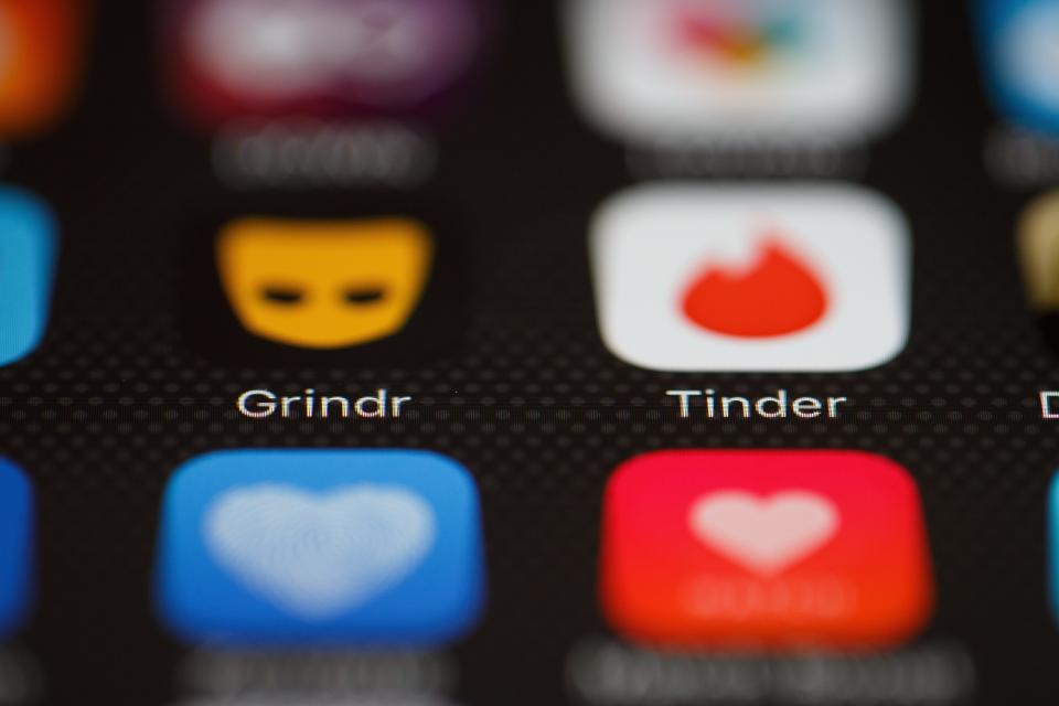 The Grindr and Tinder app logos are shown on a cellphone screen.