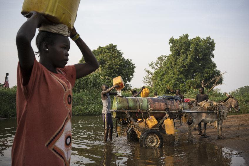 In this photo taken Thursday, March 9, 2017, a woman carries a jerrycan of river water back to her home, as young men fill water tanks from the river to take back and sell in neighborhoods around Torit, in South Sudan. As World Water Day approaches on March 22, more than 5 million people in South Sudan, do not have access to safe, clean water, compounding the problems of famine and civil war, according to the UNICEF. (Mackenzie Knowles-Coursin/UNICEF via AP)