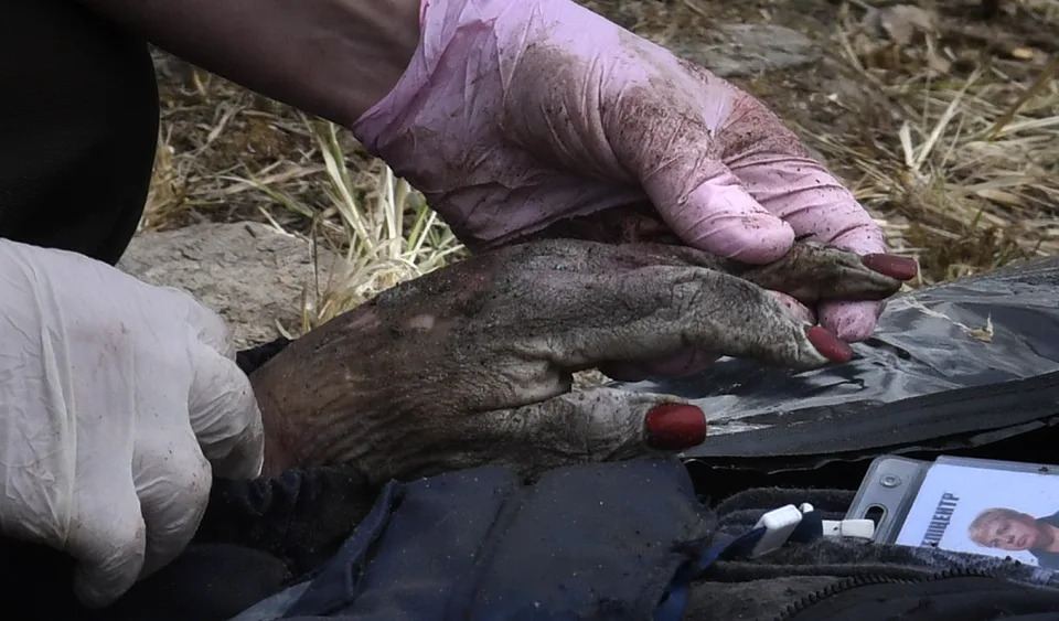 A worker holds a victim's hand with red painted fingernails as the body is carefully placed into a black body bag on April 8 in Bucha.