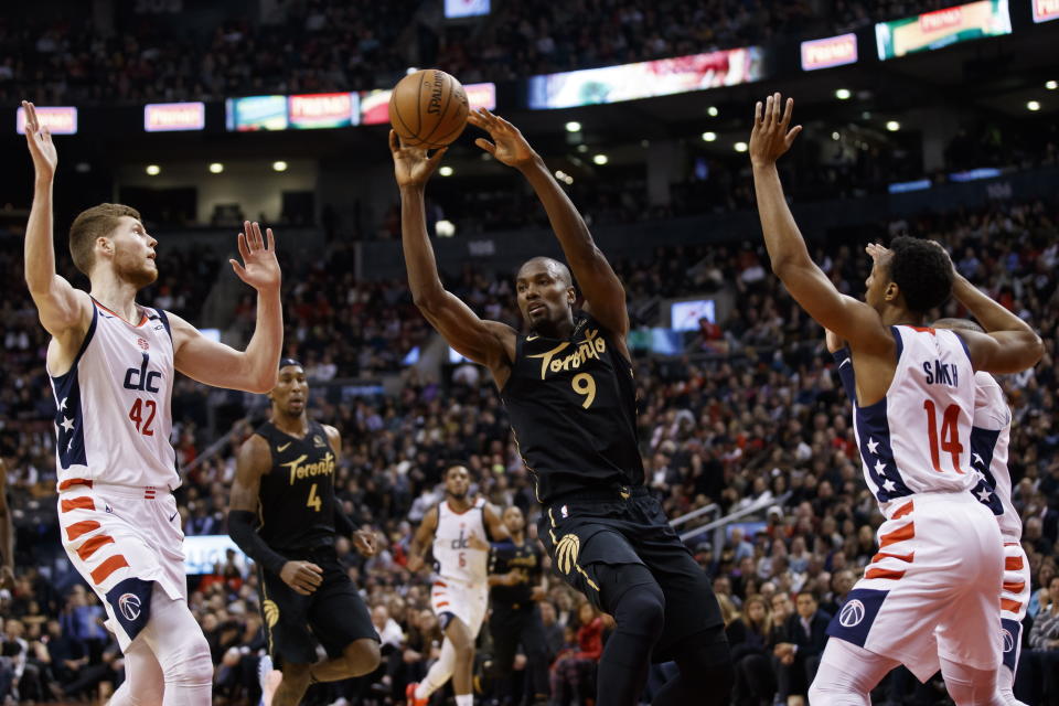 Toronto Raptors forward Serge Ibaka (9) looks to make a pass as he's defended by Washington Wizards forward Davis Bertans (42) and guard Ish Smith (14) during the first half of an NBA basketball game Friday, Jan. 17, 2020, in Toronto. (Cole Burston/The Canadian Press via AP)