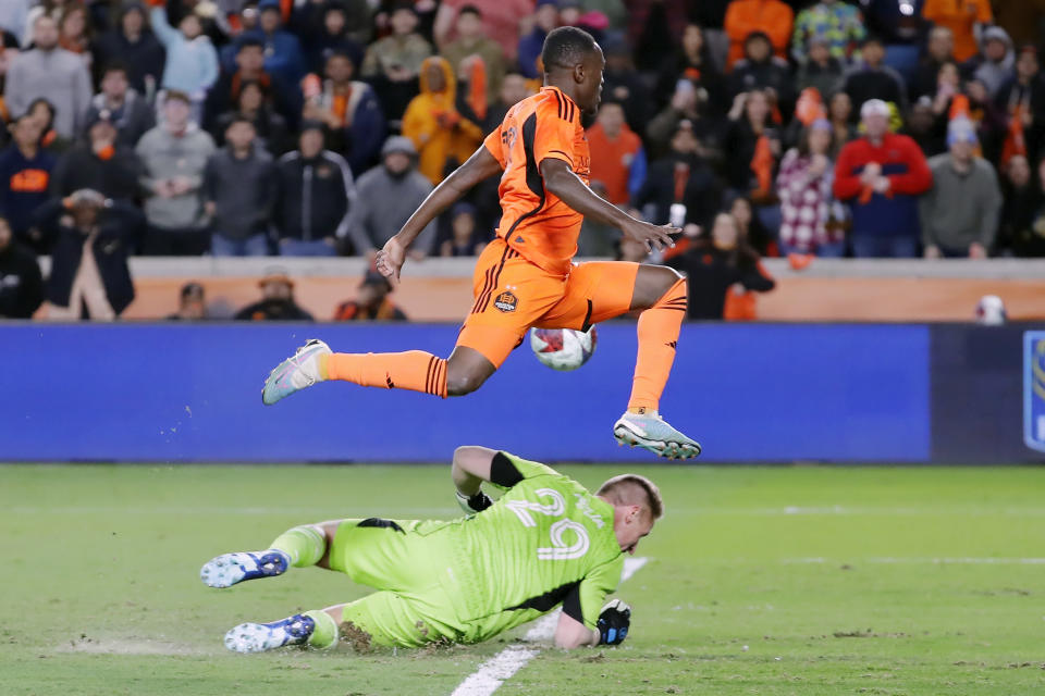 Houston Dynamo forward Ibrahim Aliyu, top, jumps over Sporting Kansas City goalkeeper Tim Melia (29) who makes a stop on a goal-attempt by Aliyu during the second half of an MLS playoff soccer match Sunday, Nov. 26, 2023, in Houston. (AP Photo/Michael Wyke)