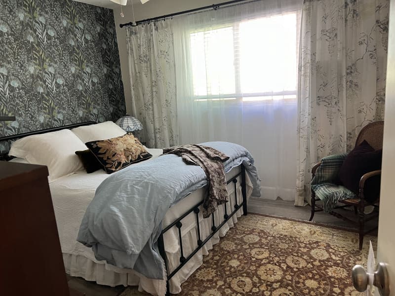 Bedroom with botanical wallpaper and other floral details and curtains covering air conditioner