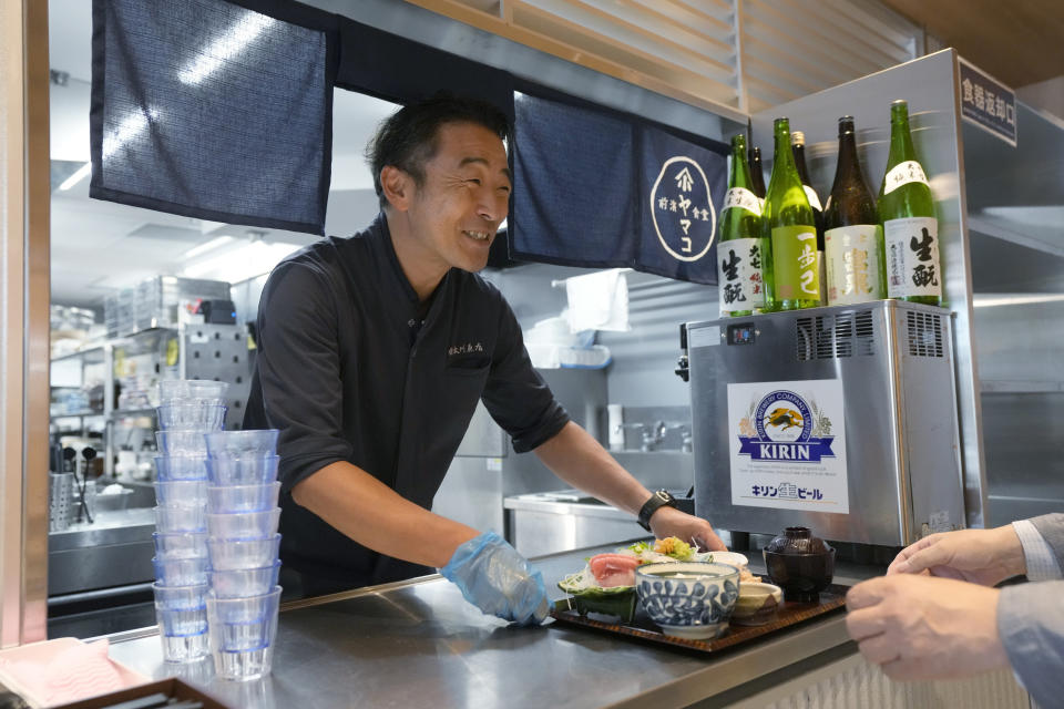 Katsumasa Okawa, owner of Okawa Fish Store, serves a fish dish to a customer at his restaurant in Iwaki, northeastern Japan on Friday, Aug. 25, 2023. Fish auction prices at a port south of the Fukushima Daiichi nuclear power plant Friday somehow dipped amid uncertainty about how consumers may respond a day after release to sea of treated and diluted radioactive wastewater began despite protests at home and in neighboring countries. (AP Photo/Eugene Hoshiko)