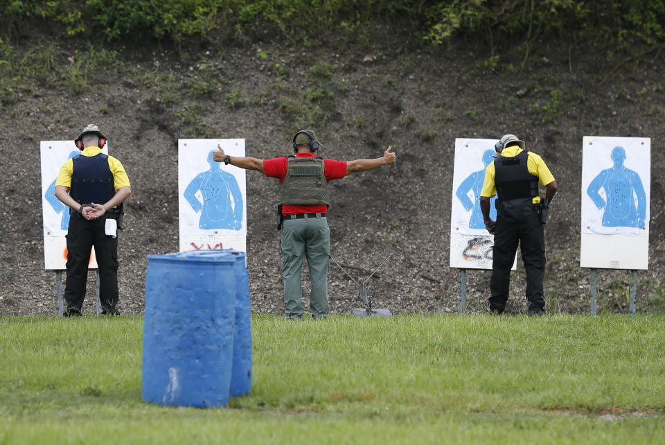 In this Monday, July 30, 2018 photo, a Broward Sheriff's Office (BSO) trainer, center, signals at the ready as he is flanked by two Broward County Public Schools newly-hired armed guardians during firearms training at BSO's gun range at Markham Park in Sunrise, Fla. Twenty-two of the Florida school districts are supplementing officers with "guardians" - armed civilians or staff. They are vetted, receive 132 hours of training and must attain a higher score on the state firearms test than rookie police officers. (AP Photo/Wilfredo Lee)