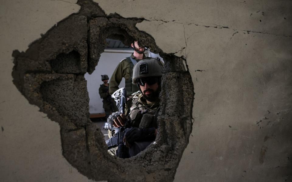 An Israeli soldier looks through a hole in the wall as he operates