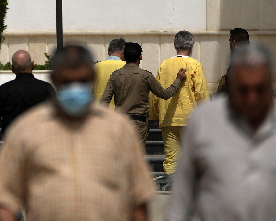 Jim Fitton, center right and Volker Waldman, center left, are handcuffed outside a courthouse in Baghdad, Iraq, Monday, June 6, 2022. The Iraqi court sentenced Fitton, a British citizen, to 15 years in prison on charges of smuggling artifacts out of the country. A German national tried with Fitton was found not to have had criminal intent in the case and will be released. (AP Photo/Hadi Mizban)