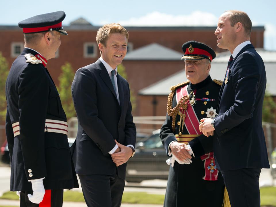 Hugh Grosvenor standing on a lawn while talking to Prince William and two other men who are dressed in official uniform.