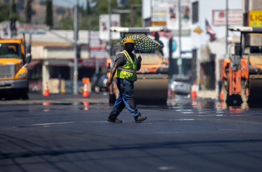 Woodland Hills, CA - July 27: Heat radiates up off fresh asphalt as a LA City street services worker carries an umbrella to ward off the sun as crews lay down new pavement on Ventura Blvd. on Thursday, July 27, 2023 in Woodland Hills, CA. (Brian van der Brug / Los Angeles Times)
