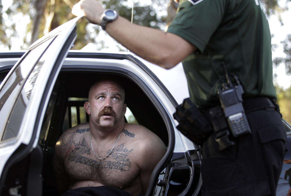 FILE - In this Oct.16, 2011 file photo Andrew Lozano, a member of the Vagos motorcycle gang, talks to a Fontana police officer after he was arrested in an early morning raid in Fontana, Calif. Closing arguments continued Thursday, Feb. 6, 2020, in federal court in Las Vegas for eight accused Vagos motorcycle club members standing trial in a broad criminal racketeering case stemming from a gunfight in 2011 with rival Hells Angels that left one person dead and two wounded at a northern Nevada casino. Defense attorneys maintain that prosecutors haven't proved their case. Prosecutors accuse the Vagos of years of acts of murder, robbery, extortion, kidnapping and drug dealing in California, Arizona, Hawaii, Oregon, Utah and Nevada.(AP Photo/Jae C. Hong,File)