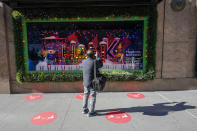 Red dots mark the spots for viewing the holiday windows display at the Macy's flagship as a man takes a photo, Friday, Nov. 20, 2020, in New York. Macy's 2020 holiday windows honors essential workers and first responders during the coronavirus pandemic. (AP Photo/Mary Altaffer)