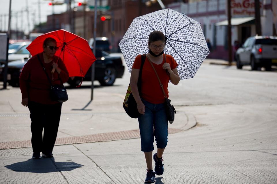 Two women use umbrellas to protect themselves from the sun as they walk around Downtown El Paso on June 20.