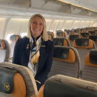 Flugbegleiterin Daniela sitzt auf der Armlehne einer Sitzreihe in einem Kurzstrecken-Airbus von Condor und lächelt.