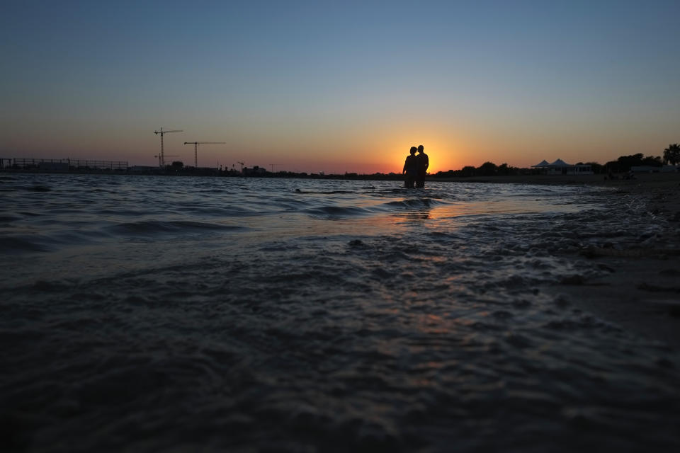 A couple stand in the sea during sunset in coastal resort of Ayia Napa in the eastern Mediterranean island of Cyprus, Saturday, Aug. 22, 2020. Meanwhile, Health Minister Constantinos Ioannou has extended until Jan. 15, 2021, a ban on outdoor festivals, concerts and exhibitions in places without seating where social distancing rules can't be enforced. (AP Photo/Petros Karadjias)