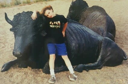 A young girl wearing an 'NSYNC T-shirt and shorts and kneeling against a large bull statue