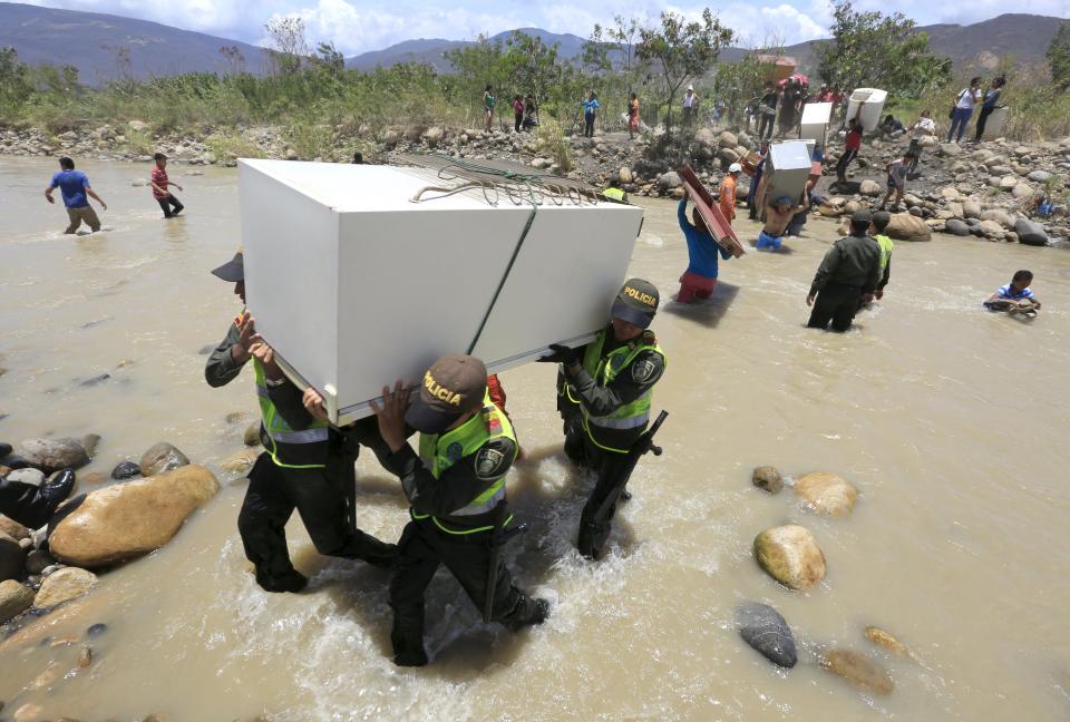 Colombian policemen carry items belonging to people arriving in Colombia while crossing the Tachira river border with Venezuela, near Villa del Rosario village