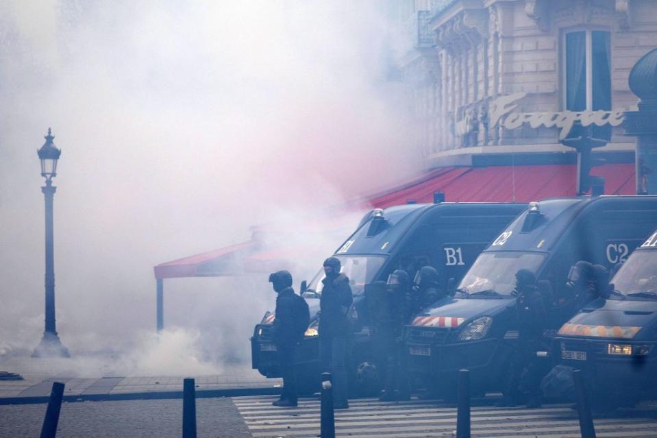 Smoke fills a street with riot police and police vans in foreground