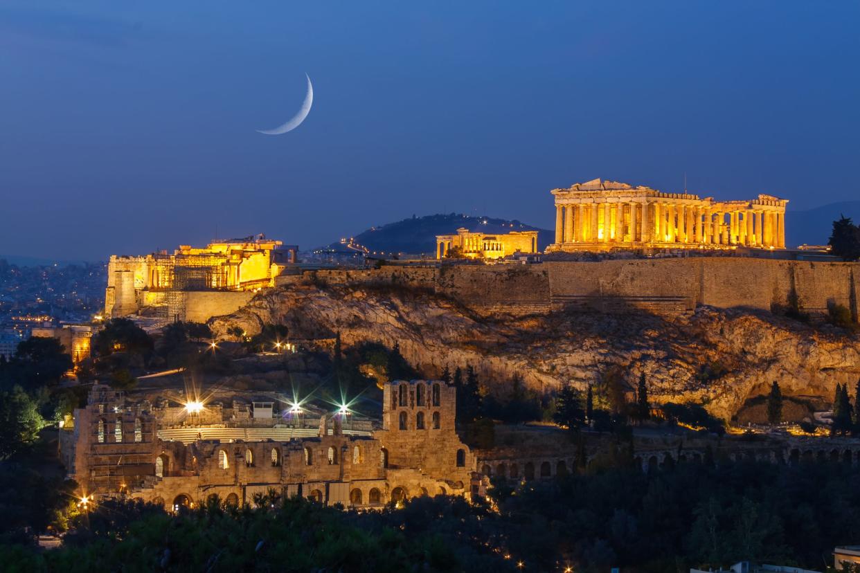 Parthenon and Herodium construction in Acropolis Hill in Athens, Greece shot in blue hour with the moon rising above the sky