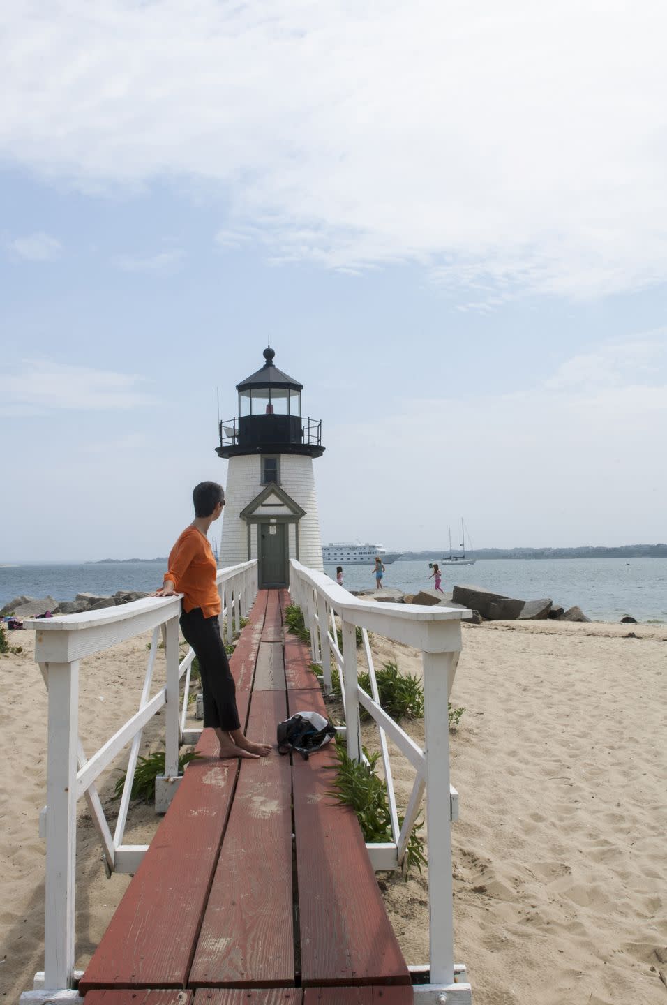 woman on walkway over beach leading to lighthouse with figures in the background