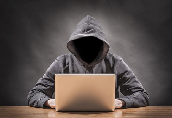 A faceless hacker in a hoodie working on a laptop.