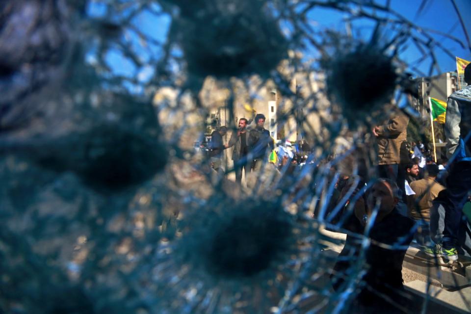 Shiite militia supporters are seen through a broken window of a checkpoint in front of the U.S. embassy, in Baghdad, Iraq, Tuesday, Dec. 31, 2019. Dozens of angry Iraqi Shiite militia supporters broke into the U.S. Embassy compound in Baghdad on Tuesday after smashing a main door and setting fire to a reception area, prompting tear gas and sounds of gunfire. (AP Photo/Khalid Mohammed)