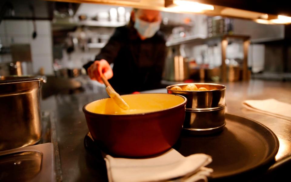 A cooker wearing a protective face mask prepare a fondue, the beloved Swiss national dish of cheese melted down with white wine in a "caquelon" pot heated by an open flame at Restaurant Marzilibruecke in Bern, on November 16, 2020. - As Switzerland contends with one of the worst coronavirus surges in Europe, the Swiss are gripped by one melting hot question: is it still safe to share a fondue? (Photo by STEFAN WERMUTH / AFP) / TO GO WITH AFP STORY BY AGNES PEDRERO AND VIDEO BY ELOI ROUYER (Photo by STEFAN WERMUTH/AFP via Getty Images) - STEFAN WERMUTH/AFP