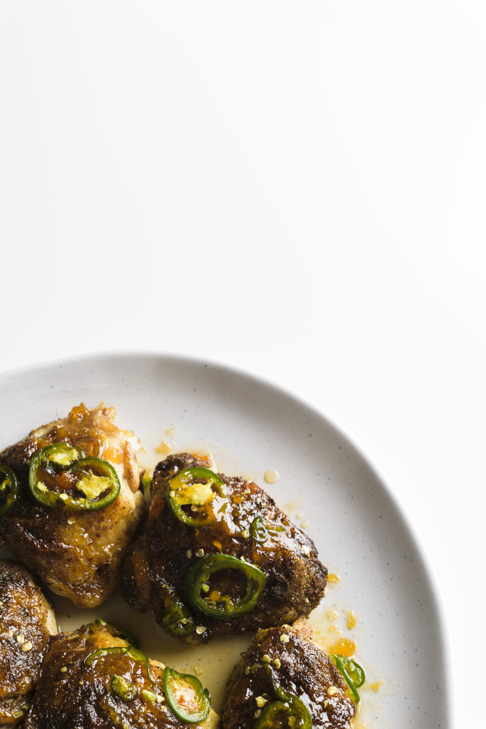 This image released by Milk Street shows a recipe for glazed chicken thighs, seasoned with jalapenos and apricot preserves. A dusting of earthy cumin on the chicken before roasting helps ground the flavors and balance the brighter sweetness of the preserves. (Milk Street via AP)