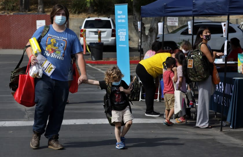 SYLMAR, CA - AUGUST 17: Ian Roistacher and his brother Mitch Roistacher, 4, walk back to their hotel room after picking up back-to-school supplies for Ian's three younger brothers during a fair at the Vagabond Inn in Sylmar on Monday, Aug. 17, 2020. The event, on the first day of school, was a partnership between Councilwoman Monica Rodriguez and L.A. Family Housing providing students with backpacks full of school supplies and other essential items for the family. The families participating are those facing economic hardship because of the pandemic. (Myung J. Chun / Los Angeles Times)