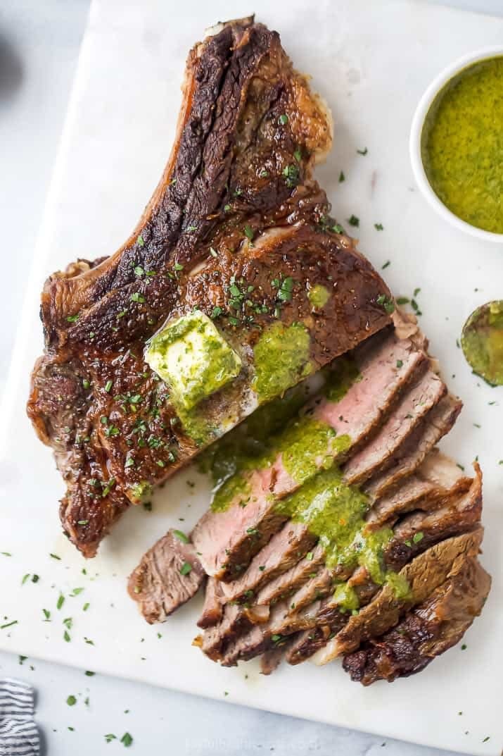 A ribeye steak sliced and topped with chimichurri.