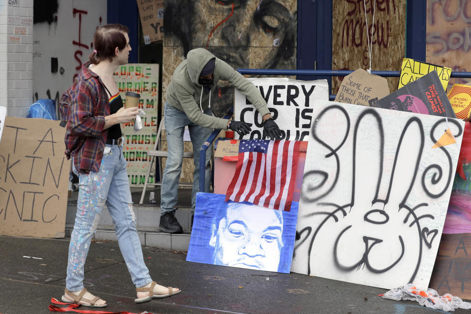 A pedestrian looks on as a person adjusts a U.S. flag displayed on the steps of the Seattle Police East Precinct building, Saturday, June 20, 2020, inside what has been named the Capitol Hill Occupied Protest zone in Seattle. A pre-dawn shooting Saturday near the area left one person dead and critically injured another person, authorities said Saturday. The area has been occupied by protesters after Seattle Police pulled back from several blocks of the city's Capitol Hill neighborhood. (AP Photo/Ted S. Warren)